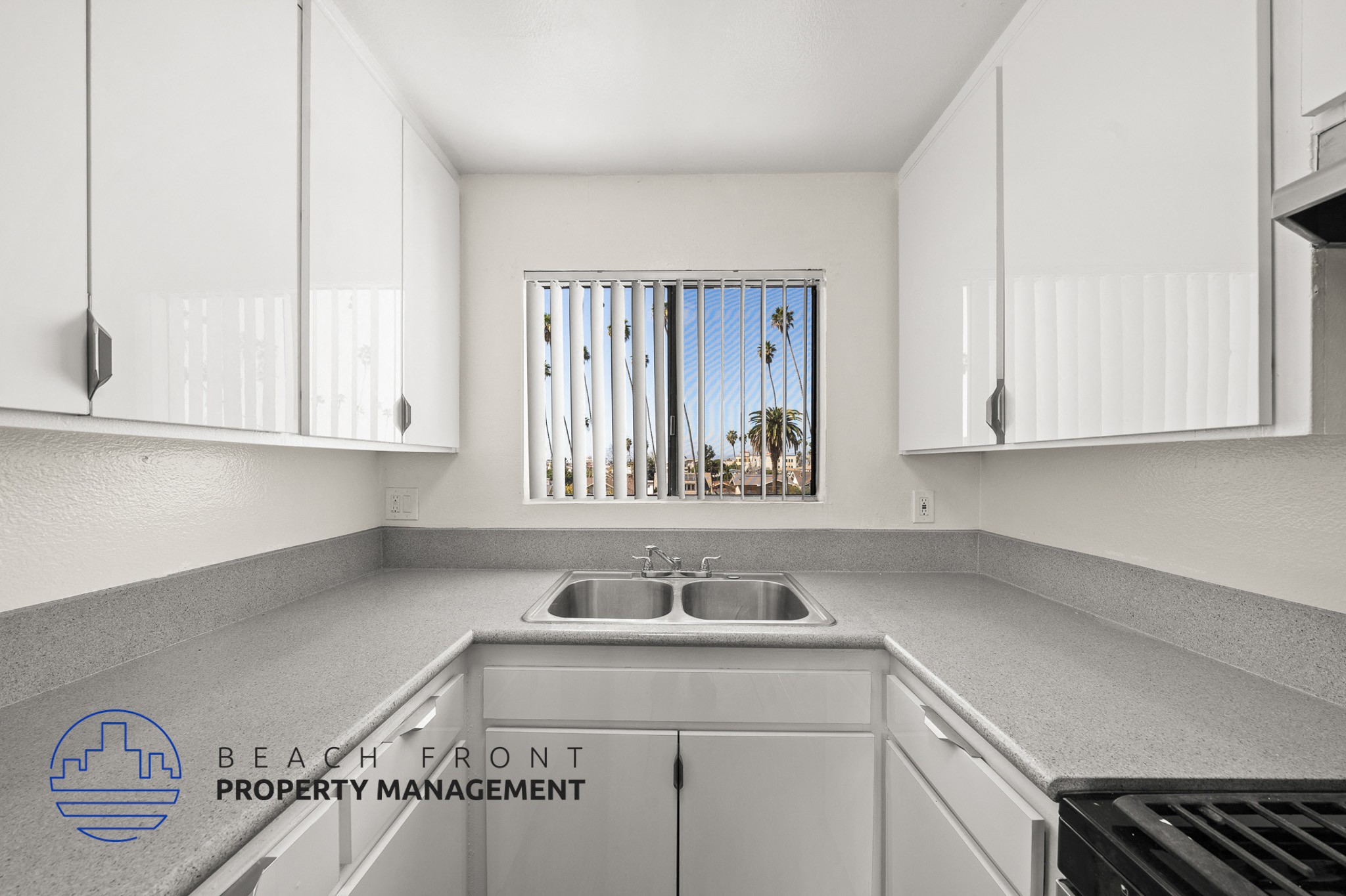 A kitchen with white cabinets and a view of a beach through the window.